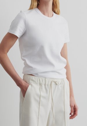 Hvid bomulds T-shirt med korte ærmer og rund halsudskæring, parret med lysebeige snoretræksbukser. Subtilt kropsnær fit.