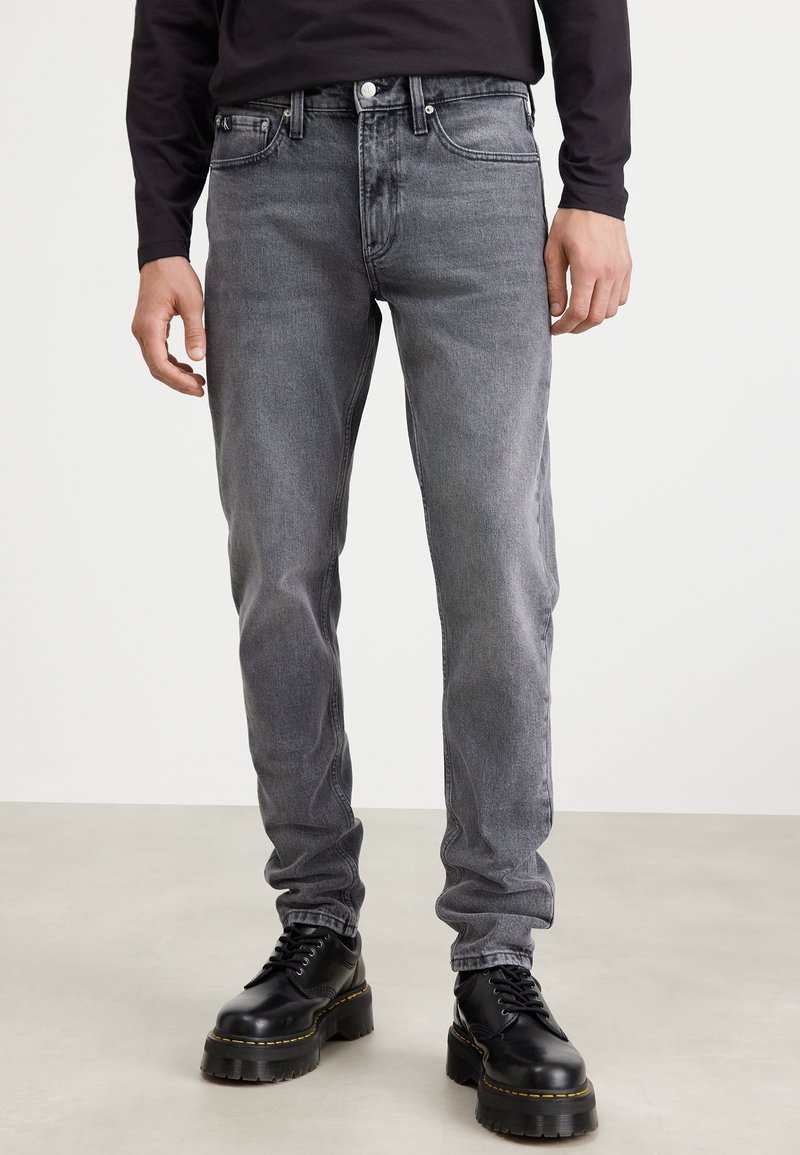Jeans en denim gris avec une coupe slim, fermeture à bouton et à zipper, design classique à cinq poches et détails de surpiqûres contrastées.