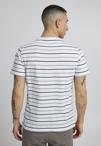 Striped t-skjorte i hvit og marineblå med korte ermer, med rund hals og slim fit. Inkluderer synlige tatoveringer på armen.