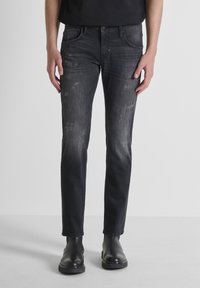 Jeans ajustados negros con una textura descolorida, que presentan detalles deshilachados y un diseño de cinco bolsillos, combinados con botas negras de tobillo.