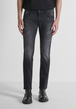 Crne slim-fit traperice s izblijedjelom teksturom, s raskuhanom detaljima i dizajnom od pet džepova, nosene s crnim gležnjačama.