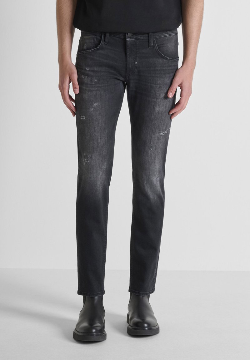 Jeans ajustados negros con una textura descolorida, que presentan detalles deshilachados y un diseño de cinco bolsillos, combinados con botas negras de tobillo.