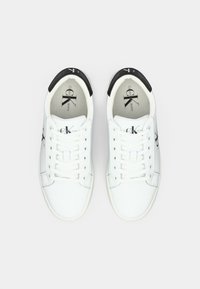 White lace-up sneakers with a black accent at the heel. Smooth material with a logo on the side and a cushioned tongue. Classic design.