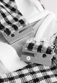 Schwarz-weiße Stoffriemen mit Muster und silberfarbenem Metallbeschlag, ausgestattet mit zwei Verschlüssen und einer weichen weißen Hintergrundstruktur.