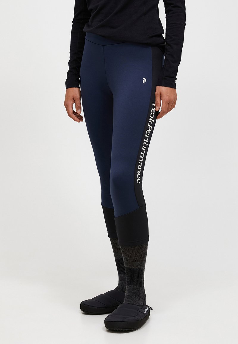 Leggings blu navy con una trama liscia, che presentano un pannello nero all'orlo e del bold testo bianco "Peak Performance" lungo il lato.
