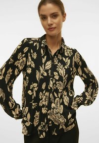 Sort bluse med cremefarvet blomstermønster, letvægts plisseret stof, lange ærmer, knaplukning foran og klassisk krave.