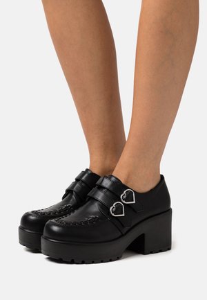 Chaussures à plateforme en cuir noir avec deux boucles de bride ornées d'accents en forme de cœur. Détail texturé sur l'avant, talon carré solide.