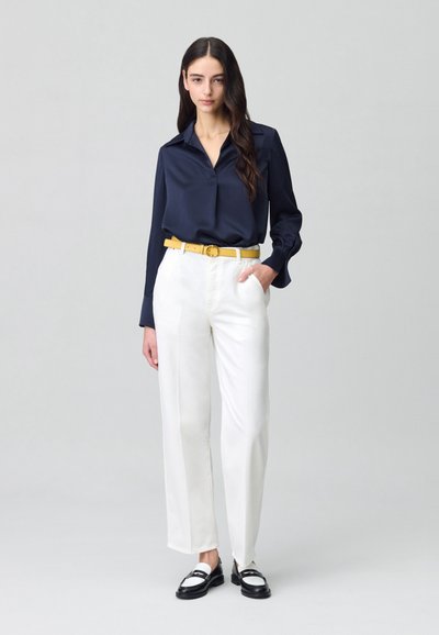 Blusa de satén azul marino de manga larga combinada con pantalones de pierna ancha blancos y un cinturón amarillo. Unos mocasines en blanco y negro completan el atuendo.