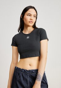 Lühikeste varrukatega, lühikese lõikega must ribidega t-särk, millel on rinnal valge Adidas'i logo. Omab ümarat kaelust ja kitsa lõiget.