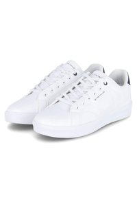 Zapatillas blancas con un upper sintético liso, punta redonda, cordones planos y un acento en contraste en azul marino en el talón. Suela ligeramente texturizada.