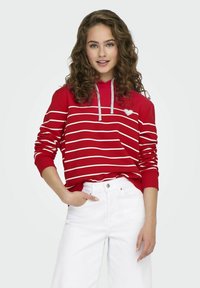 Felpa rossa con strisce orizzontali bianche, caratterizzata da una applicazione a cuore sul davanti e cappuccio con cordoncino. Abbinata a pantaloni bianchi a gamba larga.