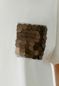 Witte t-shirt met een vierkante zak van metalen bruine pailletten. De pailletten zijn rond en laagjes, waardoor er textuur en diepte ontstaat.