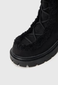 Gheata neagră de gleznă, cu partea superioară texturată și tiv din blană, șireturi negre contrastante și talpă groasă cu crampoane pentru aderență.