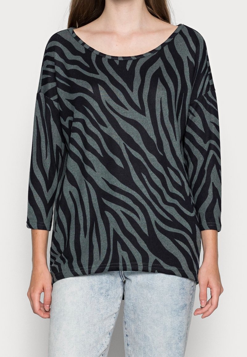 Schwarze und grüne Bluse mit Zebra-Streifen, weitem Ausschnitt und Dreiviertelärmeln, aus einem weichen, strukturierten Stoff gefertigt.