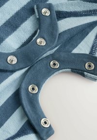 Randigt tyg i ljus och mörk blått, med tryckknappar i silverfärgade detaljer, som betonar mjukhet och textur i en böjd design.
