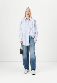 Striped long-sleeve shirt in light blue and white, paired with loose denim jeans. Model holds a small black bag, wearing light shoes.