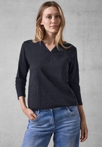 Schwarzes Langarmoberteil mit V-Ausschnitt, lockerer Passform und dezenter Stickerei, kombiniert mit hellblauen Jeans.