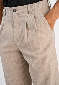 Pantalones de lana color arena con un acabado texturizado, pliegues en la cintura, cierre de botón y bolsillos laterales.