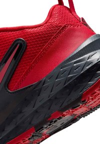 Punainen urheilukenkä, jossa on teksturoitu verkkopäällinen, mustia korostuksia ja kestävä kumipohja kuvioidulla kulutuspinnalla pitävyyttä varten.