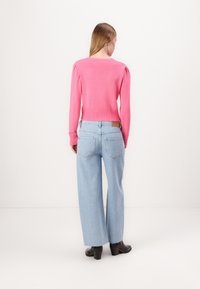 Pink knit sweater with puffed sleeves, paired with light blue wide-leg jeans. Black heeled boots complete the outfit.