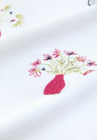 Punane vaas, millel on tikitud peened roosad õied ja rohelised varred valgel soonikust riidel.