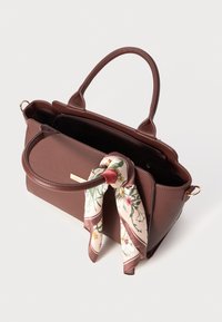 Sac à main en cuir marron avec double poignées, comportant une écharpe en soie à motif floral nouée à une poignée et un intérieur spacieux avec fermeture éclair.