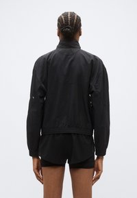 Must kerge jakk kõrge kraega, kummist mansettide ja äärega. Omadusteks on saumavaba disain ja peen logo detail tagaküljel.