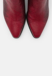 Bottines en simili cuir rouge avec un motif texturé crocodile, pointes effilées et une semelle noire lisse.
