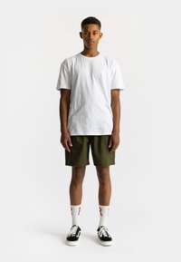 Witte katoenen t-shirt, olijfgroene shorts, zwart-witte sneakers, witte sokken met rode accenten. Eenvoudige, casual outfit zonder patronen.