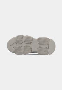 Semelle de chaussure en caoutchouc gris clair avec des motifs de bande de roulement segmentés et des rainures en chevrons pour la traction et la flexibilité, vue de dessous.