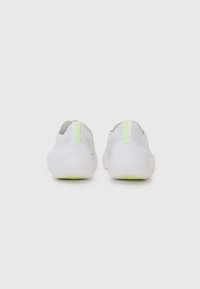 White athletic shoes with a textured upper, featuring a green accent on the heel and a thick white sole. Simple, minimalistic design.