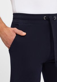 Navy sweatpants made of soft fabric, featuring an elastic waistband with a drawstring, side pocket, and smooth texture.