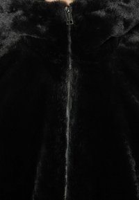 Giacca in pelliccia sintetica nera con colletto alto e chiusura centrale a zip, che presenta una texture morbida e liscia in tutto il capo.