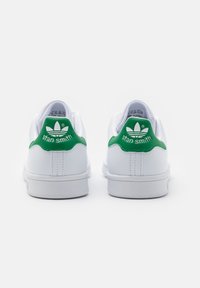Coppia di sneakers Adidas Stan Smith bianche con inserti verdi sul tallone e logo, viste da dietro su uno sfondo bianco uniforme.