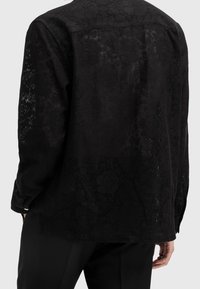 Camicia nera a maniche lunghe con un delicato motivo floreale, tessuto testurizzato e vestibilità rilassata. Polsini con bottoni e colletto classico.