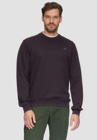 Dieppaarse sweatshirt met een ronde halslijn, geribbelde manchetten en zoom, met een klein logo op de linkerkant van de borst. Gepaarde met groene cargo broeken.