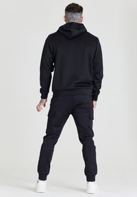 Zwarte hoodie met een kangoeroezak en een capuchon met trekkoord, gecombineerd met zwarte cargo broek met zijzakken, en witte sneakers.