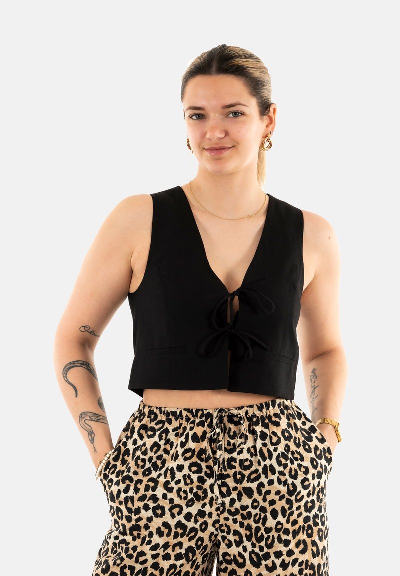 Top negro corto con escote en V y detalle de lazo en la parte delantera, combinado con pantalones beige que presentan un estampado de leopardo negro.