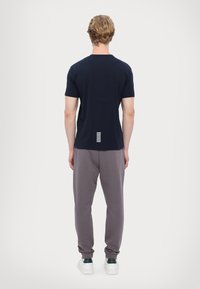 Námornícké tričko s krátkým rukávem a kulatým výstřihem, s bílými pruhy na zadní straně. Kombinováno se šedými joggingovými kalhotami a bílými teniskami.