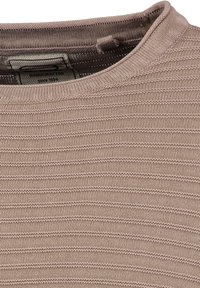 Beige gestricktes Shirt mit einem strukturierten, gerippten Design und einem runden Ausschnitt sowie einem Etikett mit der Aufschrift "Handgefertigt seit 1994."