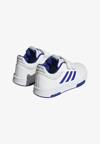 Białe buty sportowe z fioletowymi akcentami, z gładką skórzaną cholewką, wyściełanym kołnierzem i zapięciem na rzepy.