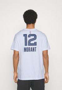 T-shirt en coton blanc à manches courtes, avec le numéro "12" en marine et "MORANT" imprimé au dos, accompagné d'un petit logo NBA en haut.