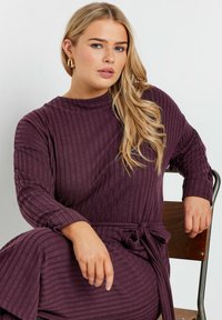 Lila ribbad klänning med långa ärmar och knytbart midjeband. Mjuk känsla och avslappnad passform, med hög halsringning och vertikala ränder.