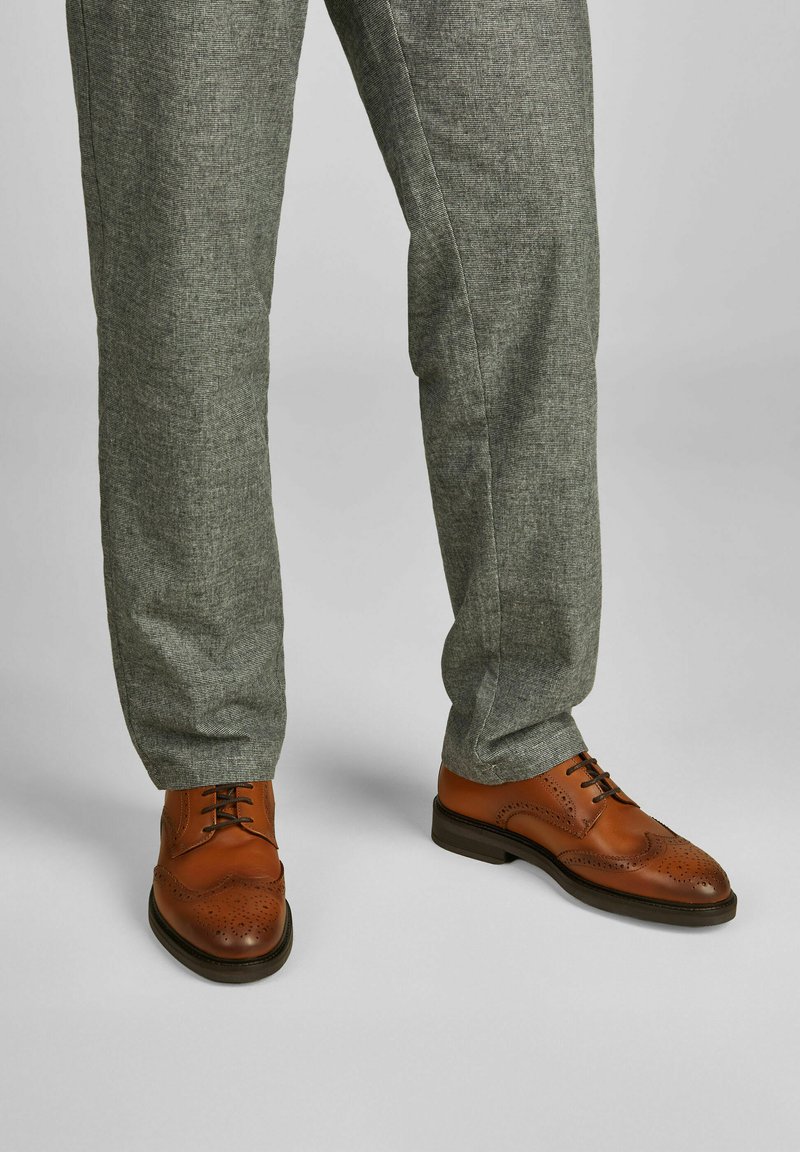Braune Leder Derby-Schuhe mit dekorativen Perforationen und runder Kappe, kombiniert mit hellgrauen strukturierten, schmal zulaufenden Hosen.