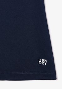 T-shirt de sport bleu marine avec une texture côtelée, portant l'inscription "ULTRA DRY" en lettres blanches près de l'ourlet. Tissu lisse conçu pour la gestion de l'humidité.