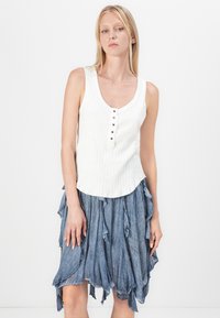 Witte geribde tanktop met een ronde hals en vijf decoratieve knopen, gecombineerd met een blauwe rok met ruffles van lichte stof.