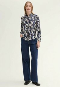 Långärmad skjorta med ett färgglatt abstrakt mönster, ihop med mörka jeansbyxor med vida ben och svarta ankelstövlar.