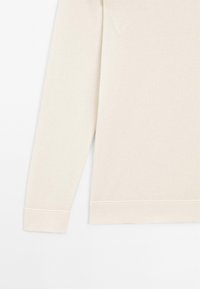Ljusbeige långärmad topp i mjukt, slätt tyg. Rundad halsringning med mudd och nederkant som har fina sömnadsdetaljer. Standard passform.