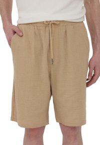 Pantaloni corti in tessuto beige e strutturato con vita elasticizzata, chiusura con cordino, due tasche laterali e vestibilità rilassata.
