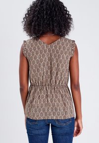 Haut marron à motifs avec manches volantées, taille élastique et col en V. Présente des imprimés géométriques en beige et brun foncé. Associé à un jean bleu.